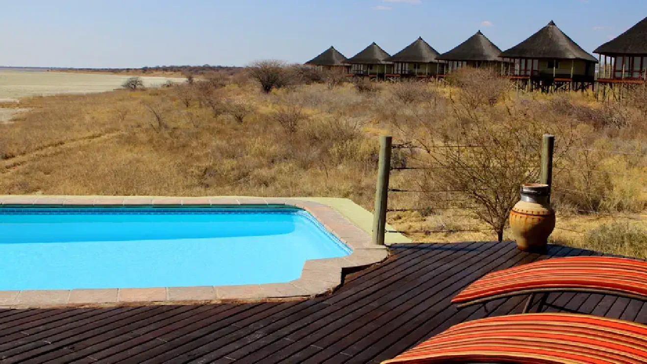 Swimming pool deck at Onkoshi accommodation overlooking Etosha Pan, with thatched chalets in the background