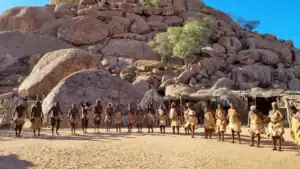 Damara Living Museum community lined up in traditional dress against the granite hills of Damaraland