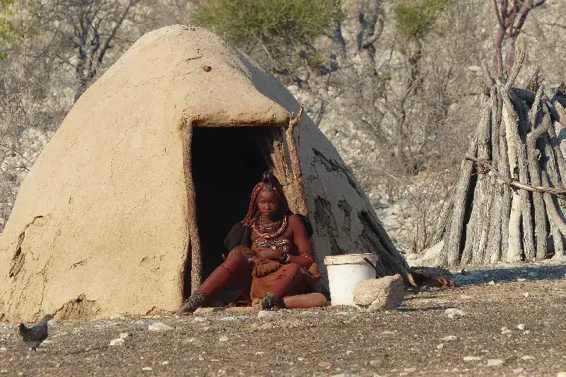 Young Himba woman seated at the entrance of a traditional clay hut in Kaokoland, Namibia