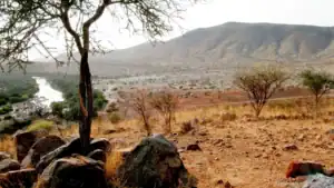 Kaokoland scenery in north-western Namibia: a rocky river lined with green trees below a broad mountain ridge