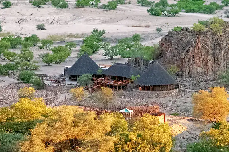 Khowarib Lodge's thatched main lodge building set against red rock cliffs in the Khowarib Gorge, Damaraland